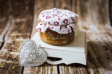 Džem Malina ve sklenici s látkovým víčkem na dřevěném stole