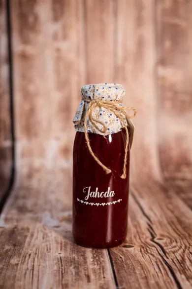 Lahev jahodového sirupu s látkovým krytem s květinovým vzorem a jutovou šňůrou na dřevěném pozadí