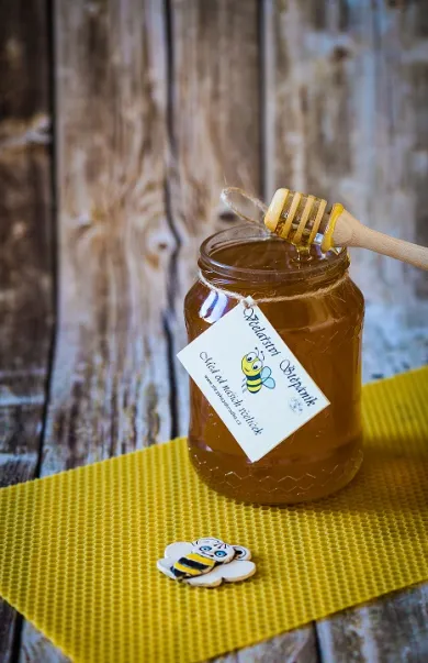 Med květový ve sklenici na dřevěné desce s dřevěnou lžičkou a žlutou podložkou