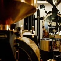 Průmyslový kávový pražič s kovovým tělem a černými mosaznými díly v továrně